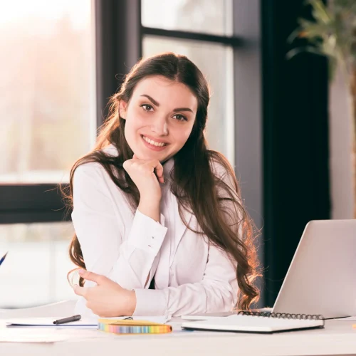 Professional translator working at desk with laptop, documents, and writing supplies in modern office environment.