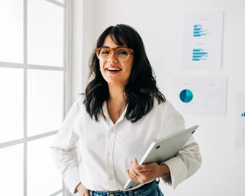 Professional woman holding tablet in bright office with business analytics charts on whiteboard